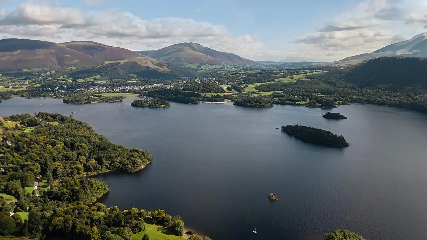 A Lake District valley from the air, with a long lake, wooded islands and the fells rising behind.